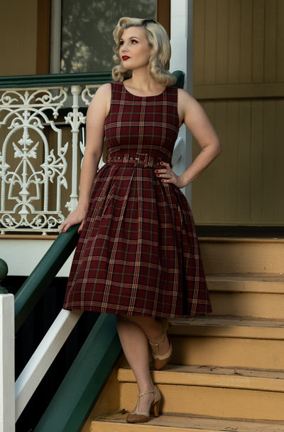 Woman wears our sleeveless Annie swing dress, in burgundy red tartan print, on some steps