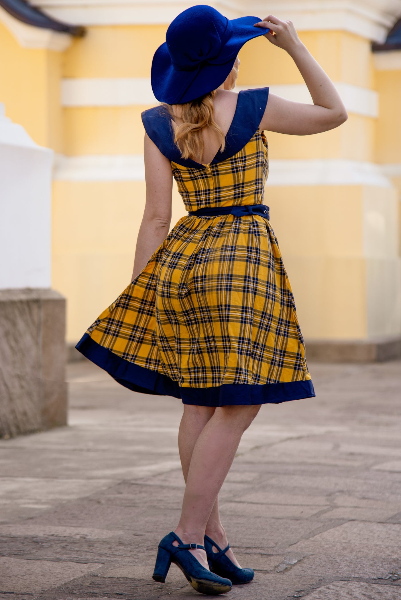 Blogger wears our sleeveless swing dress, in yellow navy blue tartan print, back view