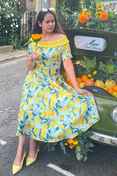 Woman wears our bateau short sleeved swing dress, in blue/yellow lemon print, on a fruit car