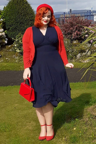Woman wearing our Elise 40's casual day dress, in dark blue, with red accessories