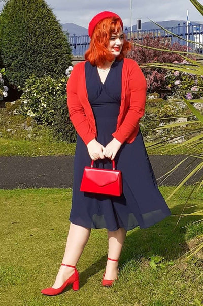Woman wearing our Elise 40's casual day dress, in dark blue, with red accessories