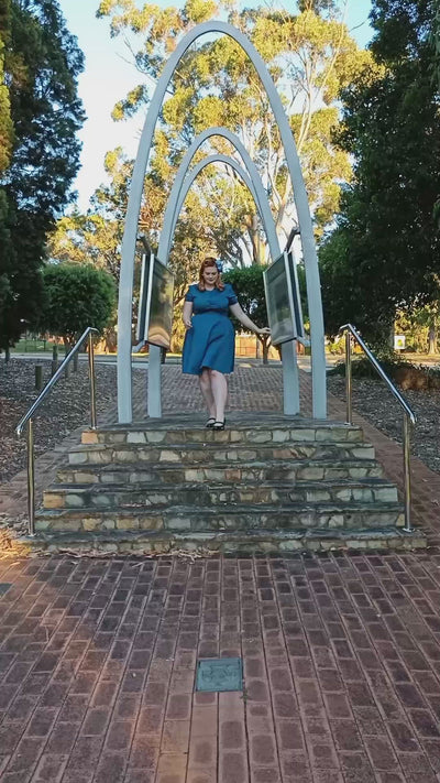 Video of a woman wearing our short sleeved Penelope button top dress in teal blue, walking down steps towards the camera