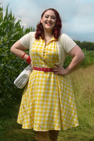 Woman wears our sleeveless button-top swing dress, in yellow/white gingham check print, in nature, with a jacket