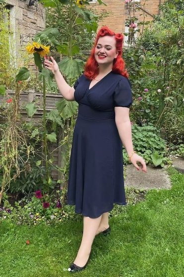 Woman wears our Elise 1940's casual day dress, in navy blue, by a sunflower