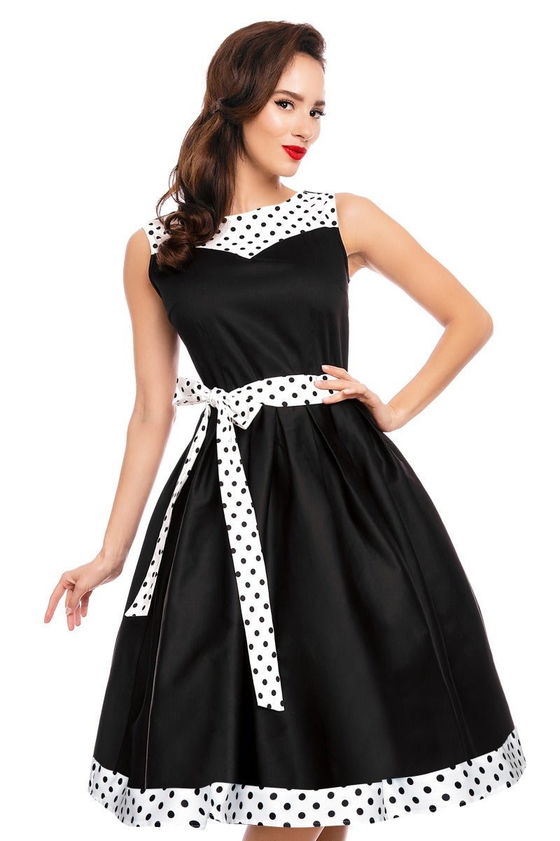 Model wears the Elizabeth flared dress, in black, with white polka dot trims and belt, front view
