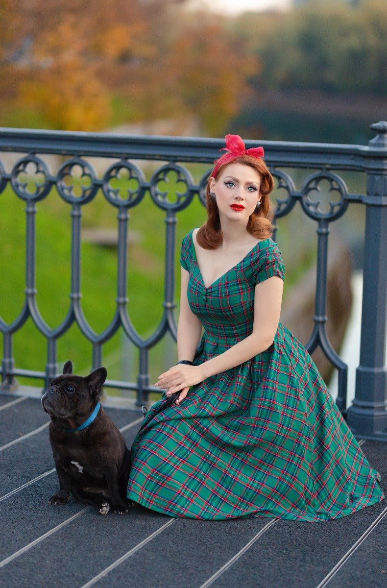 Woman wearing our short sleeved Lily dress in green and red tartan check print, with a dog, on a bridge