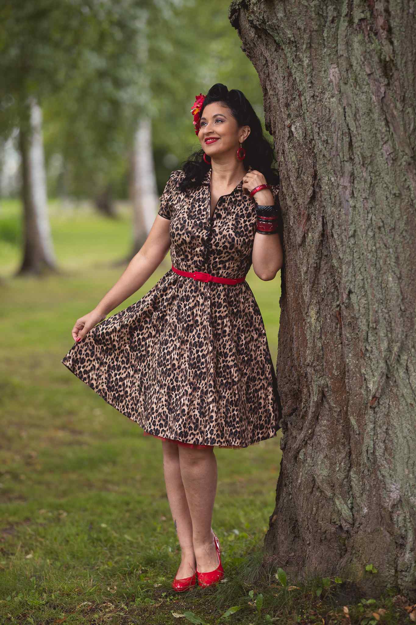 Woman wears our short sleeve Penelope dress, in brown leopard print, in a park, with trees
