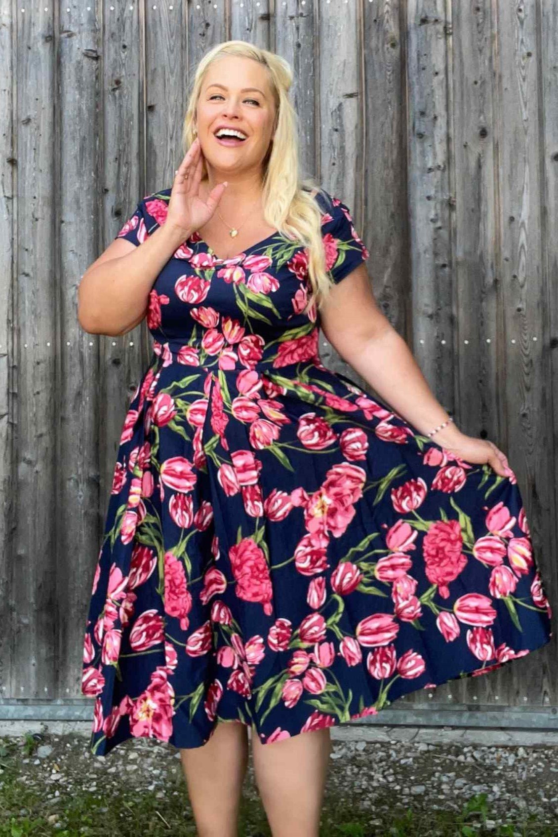 Woman wearing our V neck Lily dress, in navy blue, with pink tulips, with accessories, front view