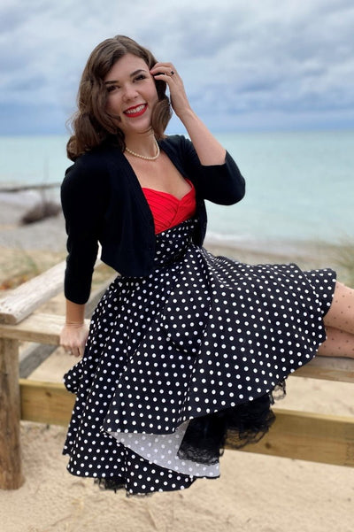 Woman wearing our Grace sleeveless dress, in black, with white polka dots, sitting down view