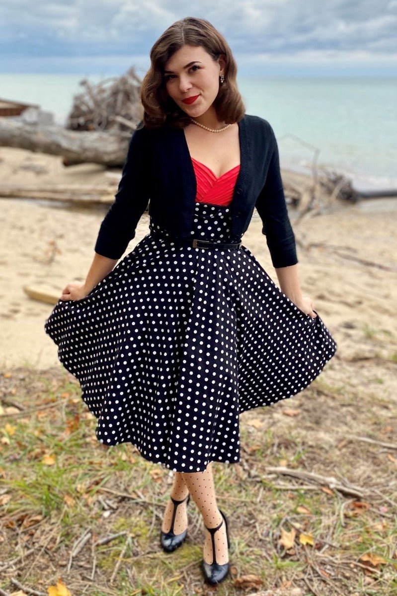 Woman wearing our Grace sleeveless dress, in black, with white polka dots, front view