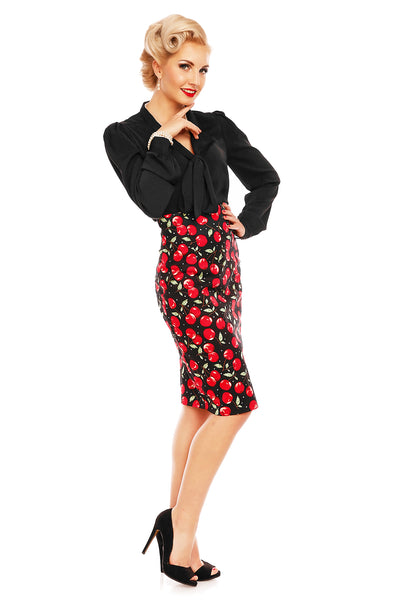 Model wears a cherry print falda pencil skirt, with cape and black top, side view