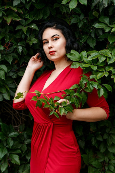 Woman wearing our Harper wrap over dress in burgundy red, in a bush