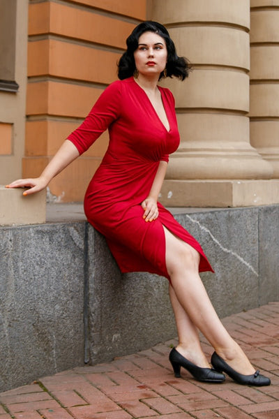 Woman wearing our Harper wrap over dress in burgundy red, against a building