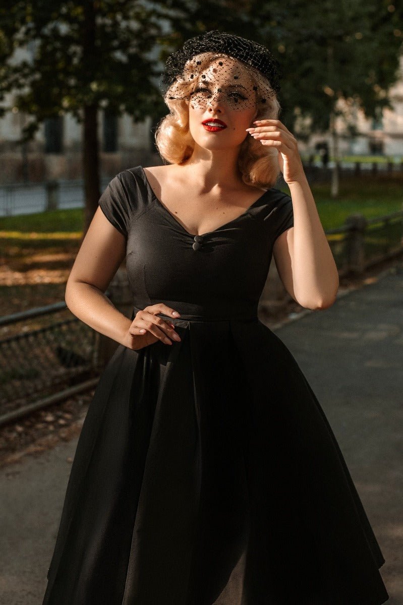Woman wearing the black Lily swing dress, with short sleeves, with black veil, in a park 