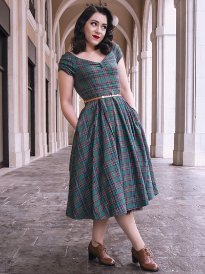 Woman wearing our short sleeved Lily dress in green and red tartan check print, with accessories, in an archway