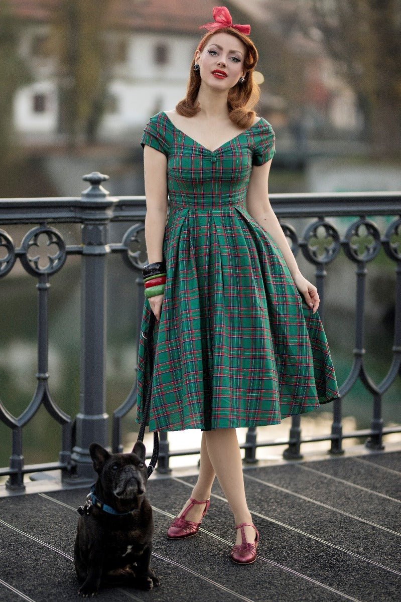 Woman wearing our short sleeved Lily dress in green and red tartan check print, with a dog, on a bridge