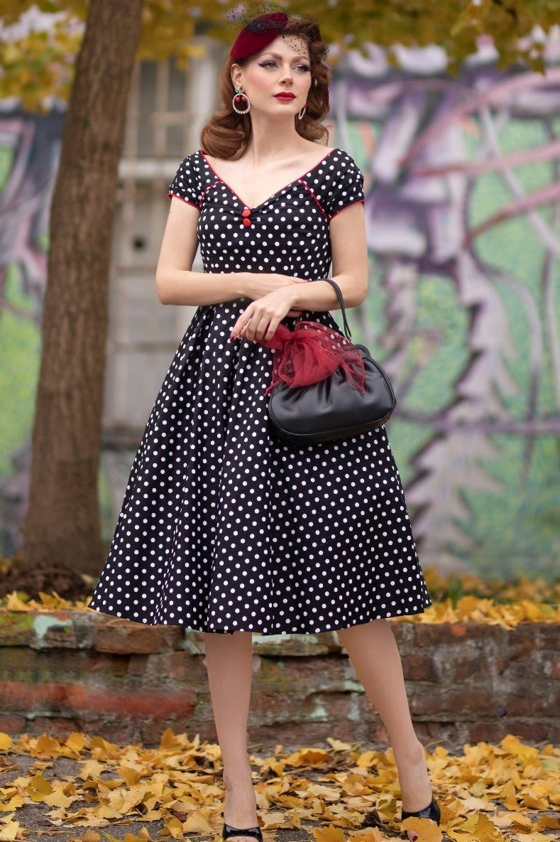 Model wears our Lily short sleeved swing dress, in black, with white polka dots, with accessories, in a park, in autumn