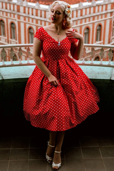 Model wears our Lily short sleeve dress, in red, with white polka dots, on a balcony, overlooking old buildings