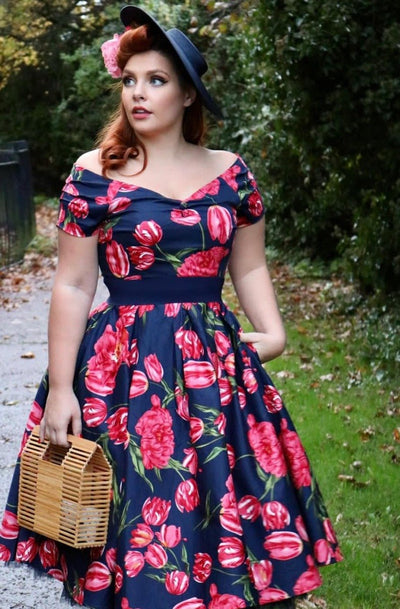 Woman wearing our V neck Lily dress, in navy blue, with pink tulips, with accessories, front view