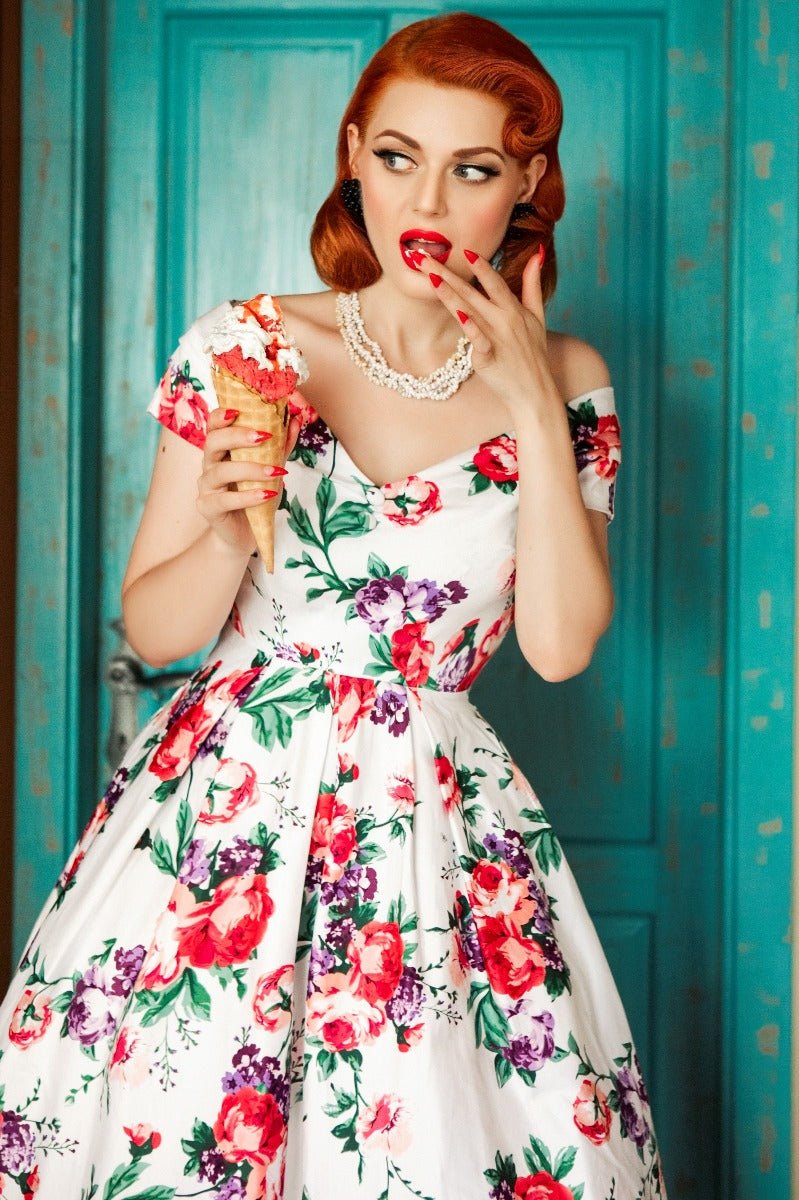 Model wearing our Lily, off-shoulder 50's Evening Dress in White, with pink and purple flowers, whilst eating an ice cream