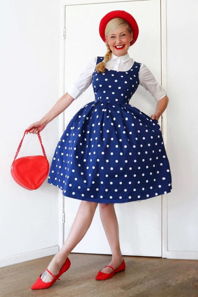 Woman wears the Amanda swing dress in dark blue, with white polka dots, with accessories, hand in pocket