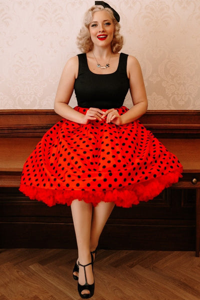 Woman wears our Sleeveless Amanda dress, with black top and red skirt, with black polka dot spots, with petticoat and hat