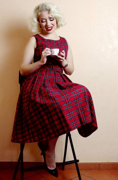 Model sitting, wearing red tartan swing dress