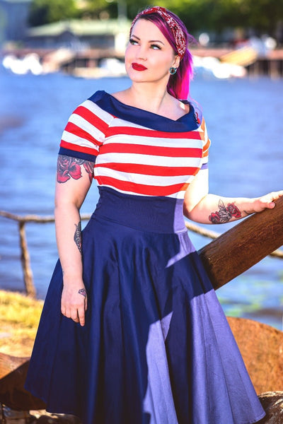 Woman wears our Darlene short sleeve dress in navy blue, with red and white stripes, in front of a boating lake
