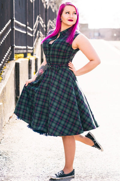 Pink haired woman wears our sleeveless Poppy button up dress in green tartan print, with a petticoat and accessories