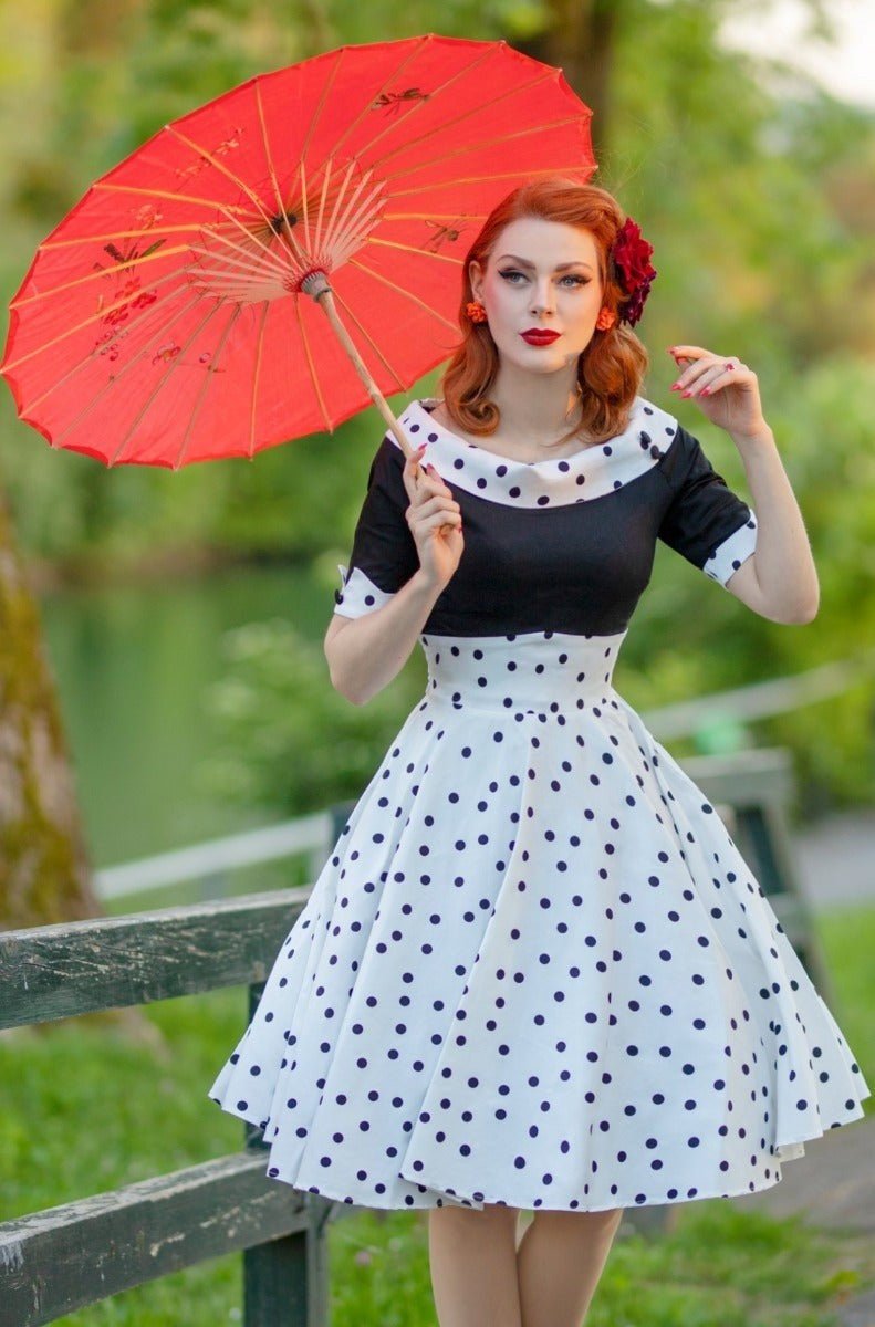 Model wearing black and white polka dot swing dress and holding a red umbrella