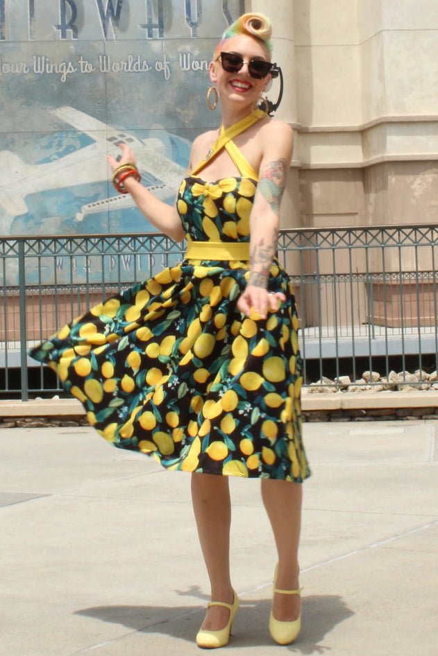 Woman wearing Sophia Halterneck Flared dress in black, with yellow lemons, with a vintage hairstyle