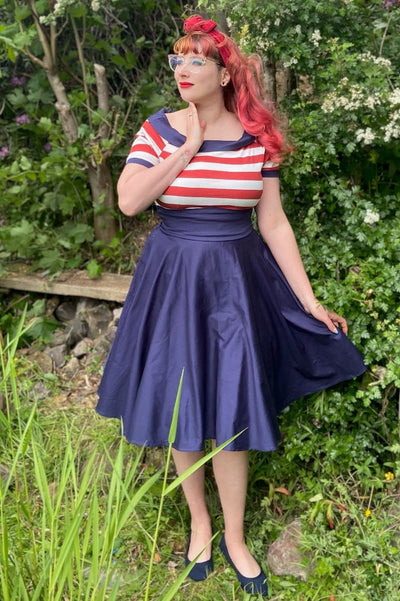 Woman wears our Darlene short sleeve dress in navy blue, with red and white stripes, in the countryside