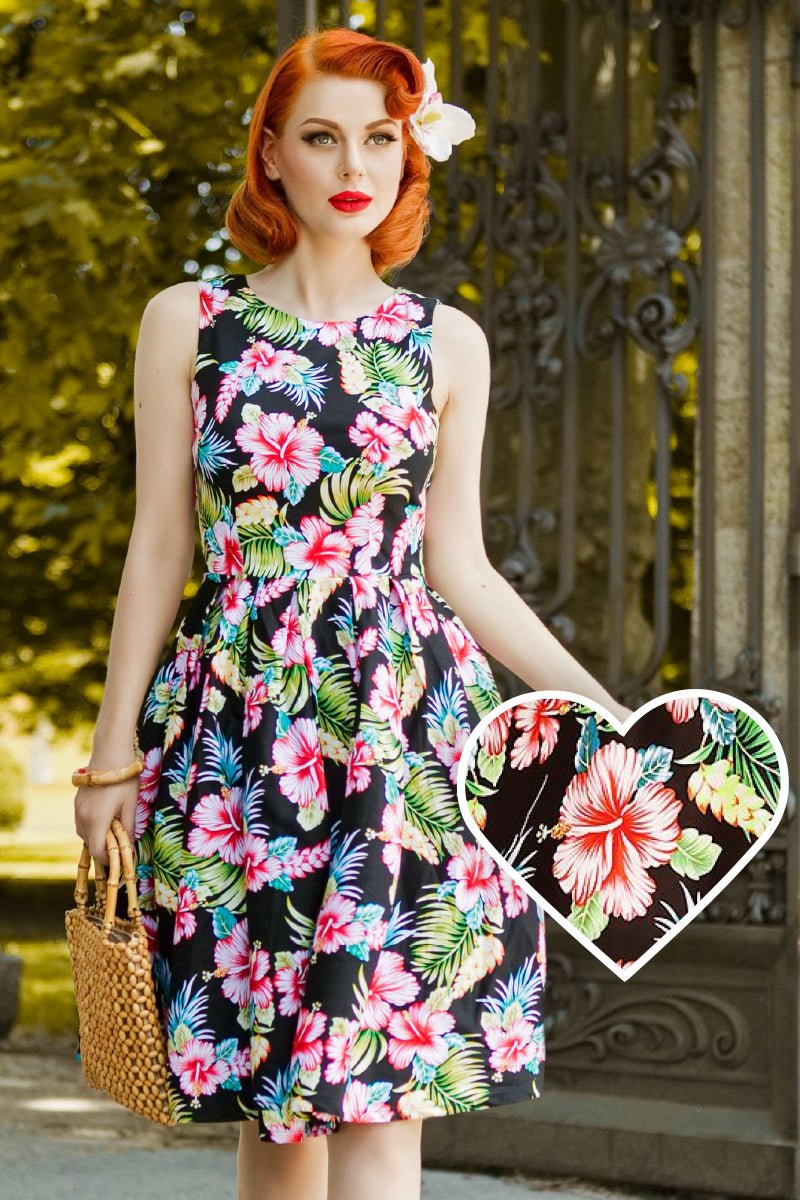 Model wearing our Annie dress, in black/pink orchid floral print,  front view, in front of gates