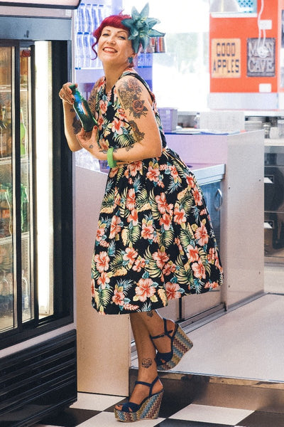 Women wearing our Annie dress, in black/pink orchid floral print, in front of a vending machine