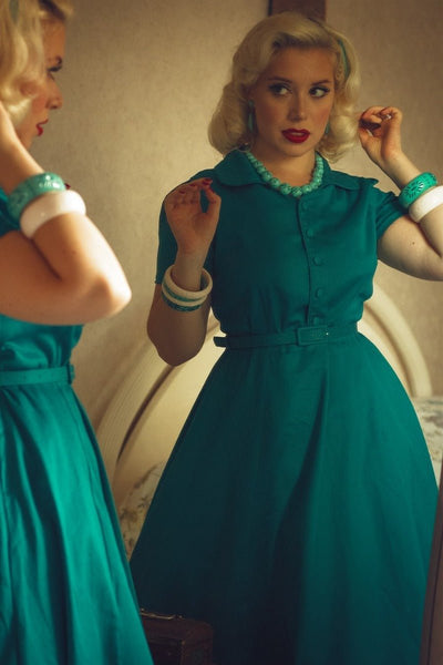 Woman wearing our short sleeved Penelope button top dress in teal blue, whilst looking in a mirror